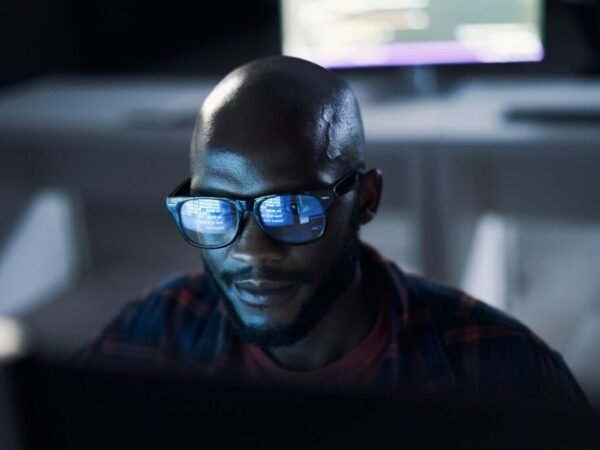 Programmer, black man and code reflection in glasses, cyber security and hacking in workplace. African American male employee, coder or IT specialist with eyewear, focus or data analysis in workplace